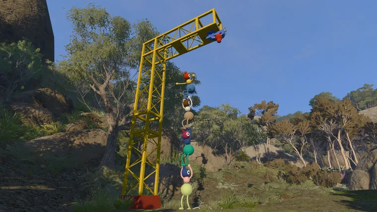 A tall yellow metal tower frame among granite boulders and eucalypts, with a chain of Big Walk characters climbing it one above another (May 2025 build)