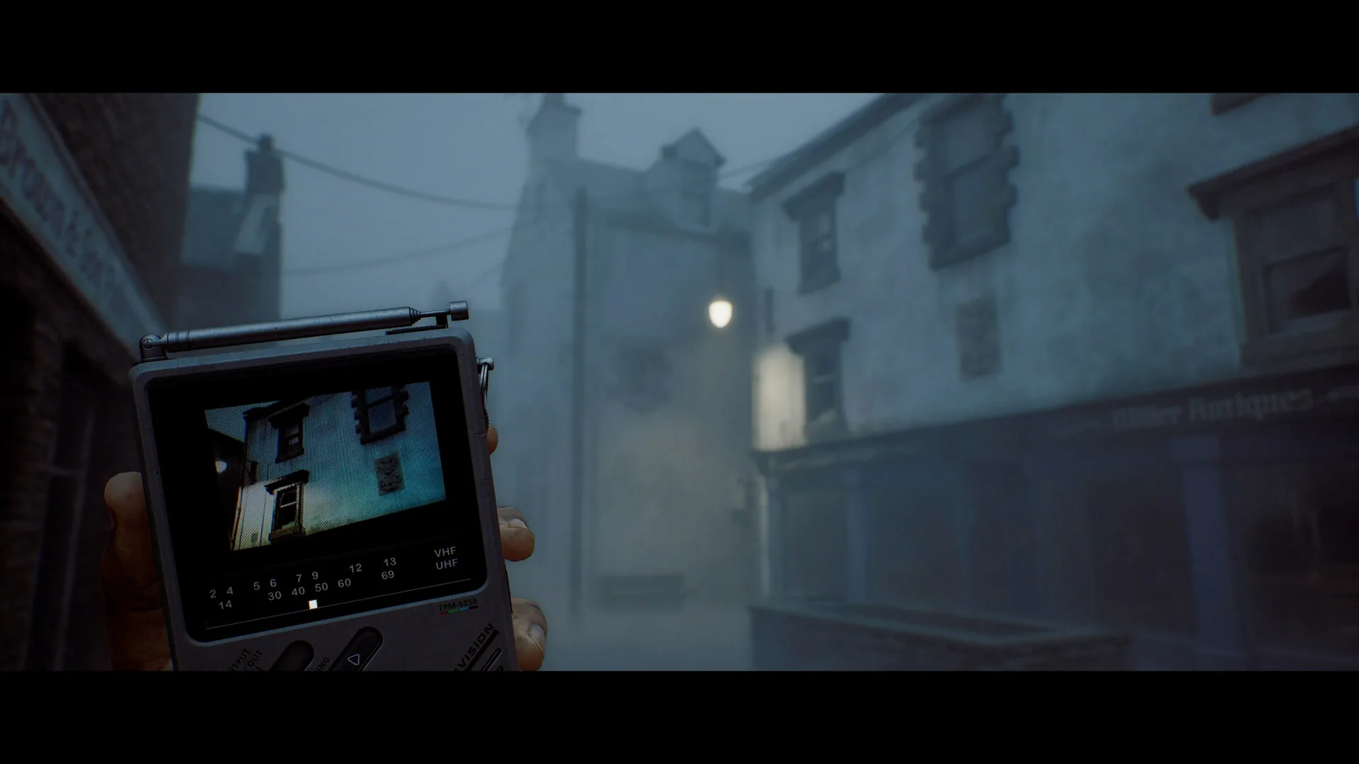A hand holding the pocket television in fog, its screen showing a nearby street facade.
