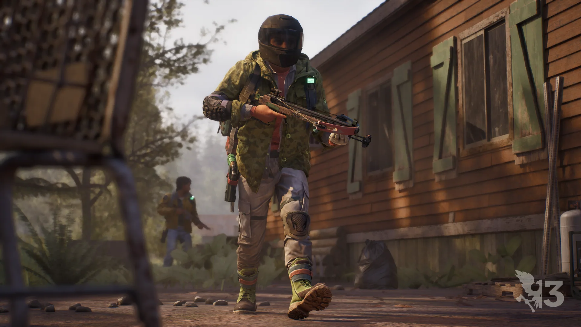 Helmeted survivor with a crossbow walking past a wooden house as a companion follows
