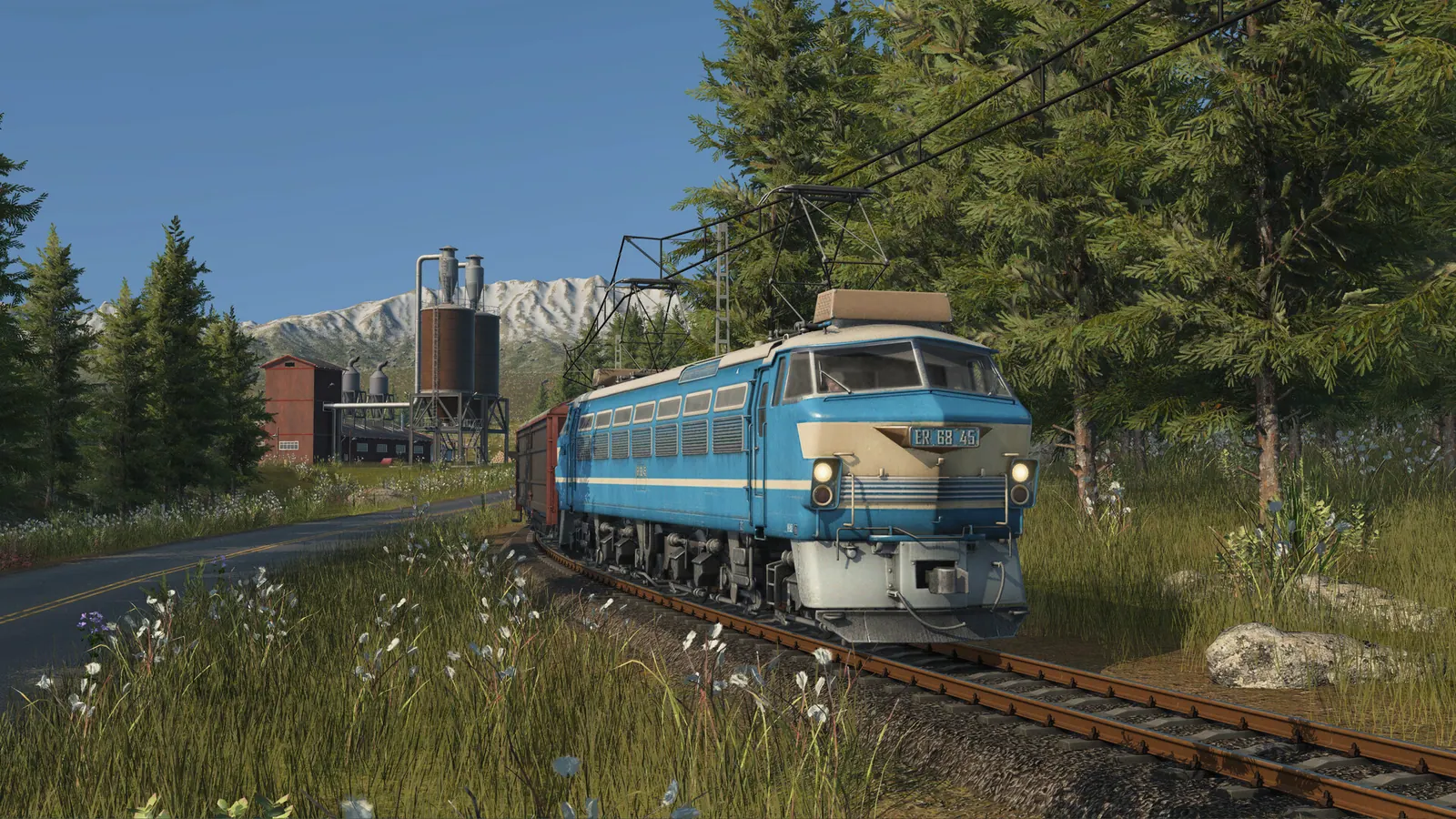 Blue-and-cream electric locomotive hauling freight through a mountain meadow